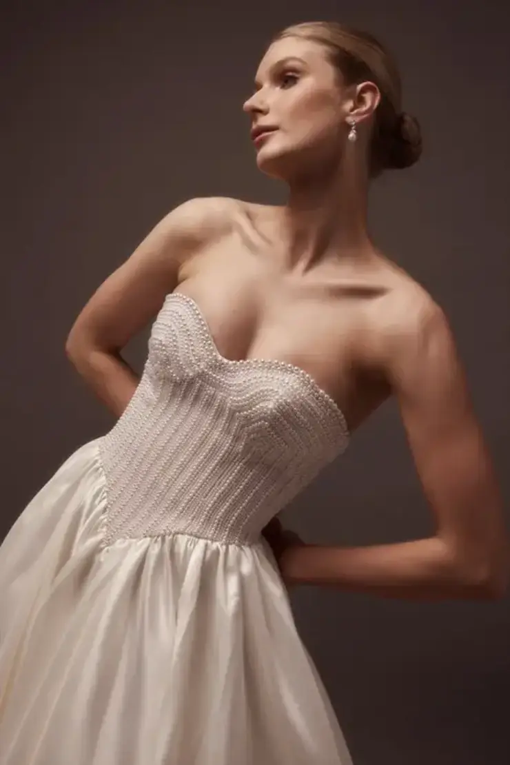 Model is wearing a mikado satin ball gown wedding dress with pearls on the bodice