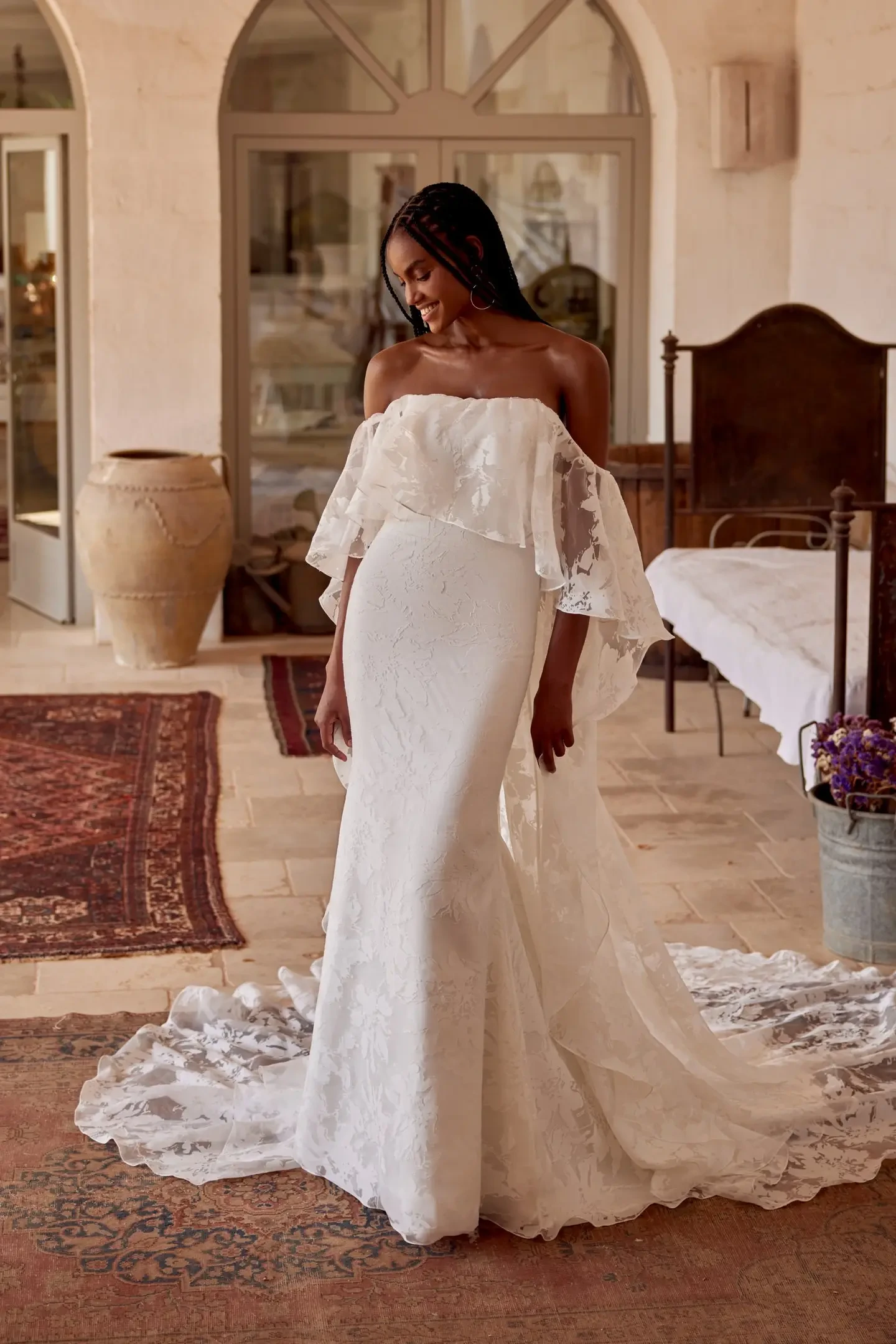 Model is wearing a strapless fit and flare gown in ivory organza jacquard with a straight neckline and chapel-length train.