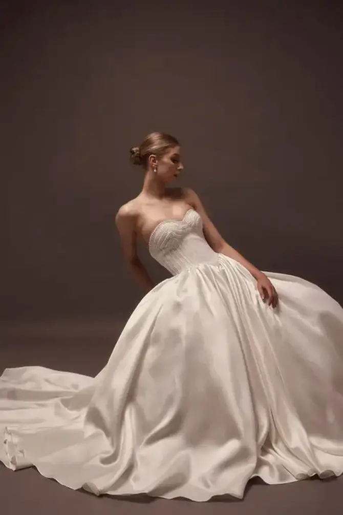 Model is wearing a mikado satin ball gown wedding dress with pearls on the bodice