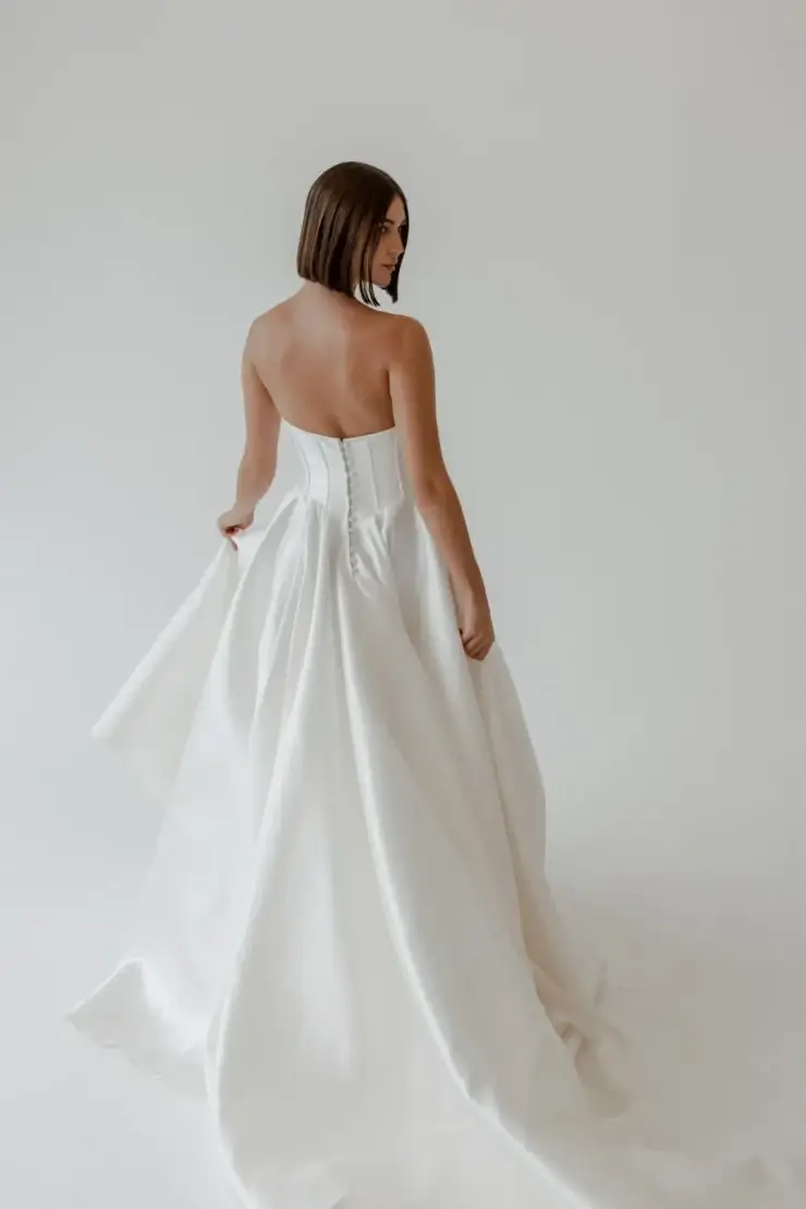 Model is wearing a strapless sleek ball gown with a pointed bodice and corset boning.