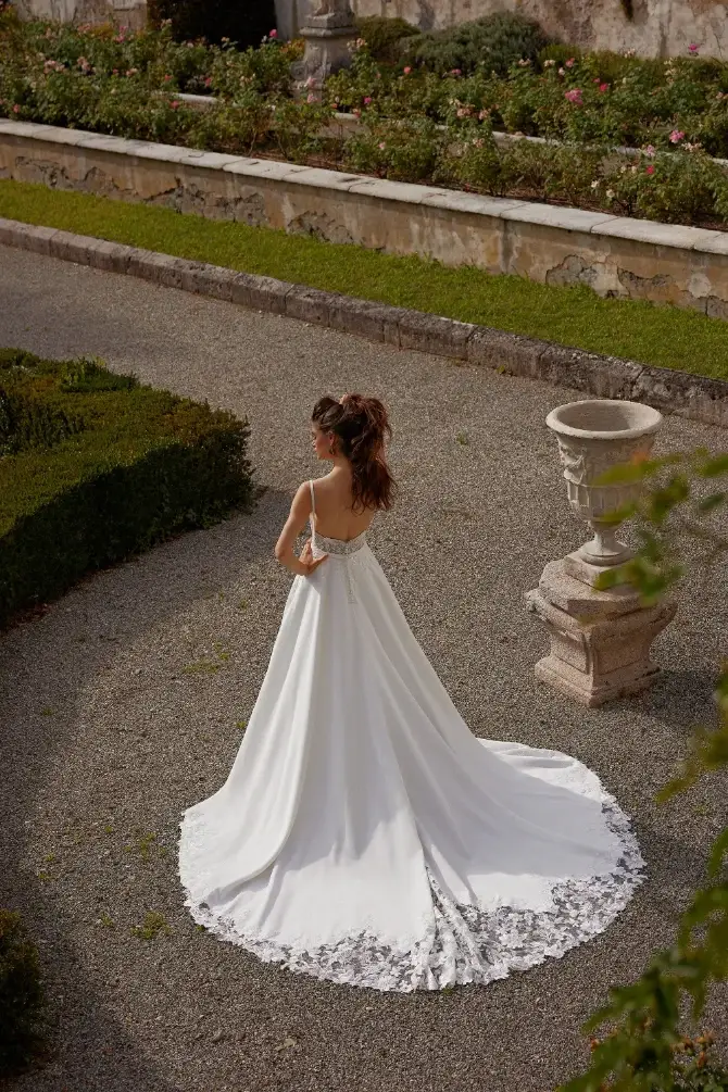 Model is wearing a satin A-line gown with a lace bodice, square neckline, and flowing skirt for a timeless rustic look.