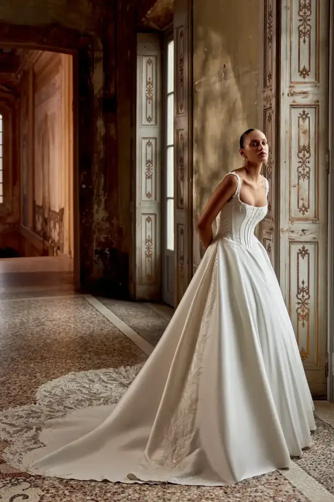 Model is wearing a mikado ball gown with a corset bodice and basque waist with a square neckline 