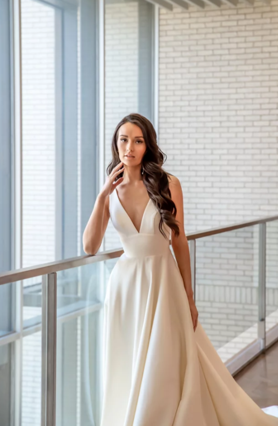 Model is wearing a dove satin gown featuring a flattering v-neck bodice, wide waistband, and illusion v-sides.