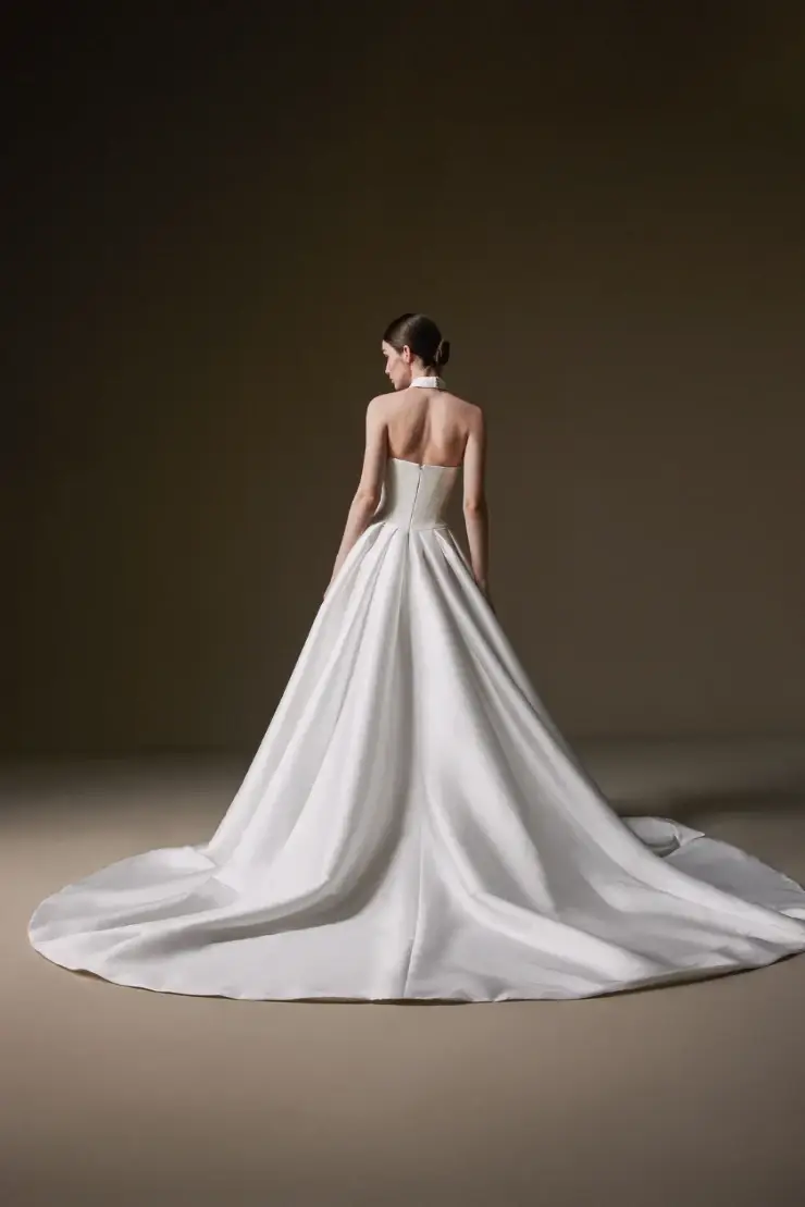 A woman stands elegantly in a strapless white gown with a long, flowing train. The smooth fabric creates a sense of sophistication and grace.