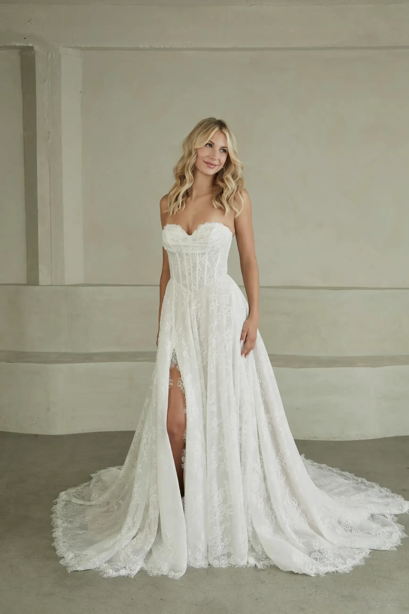 Model is wearing a romantic Chantilly lace gown with a sweetheart neckline, off-shoulder cap sleeves, flowing lace skirt, and side seam pockets.